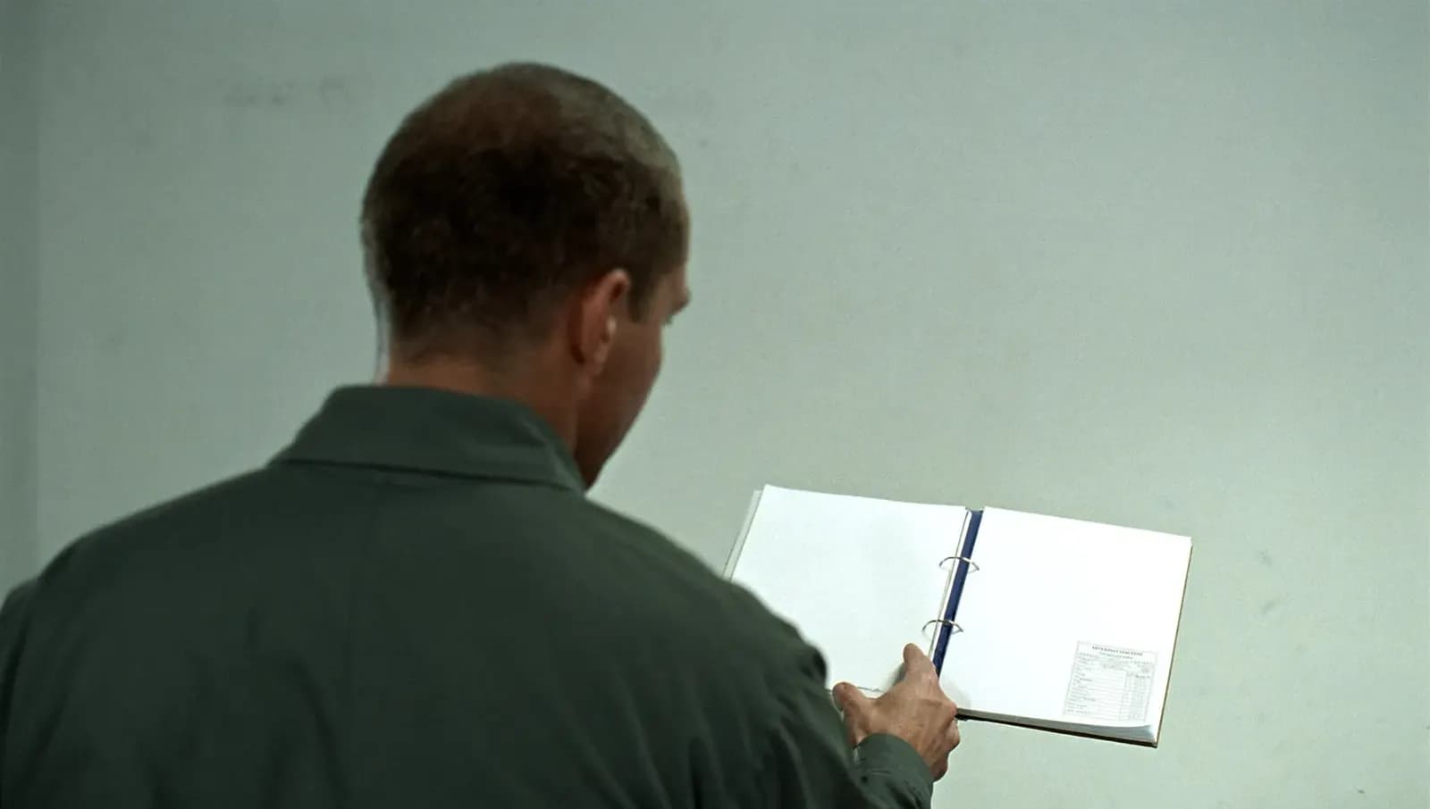 A security specialist, seen from behind, reading a binder against a bare wall.
