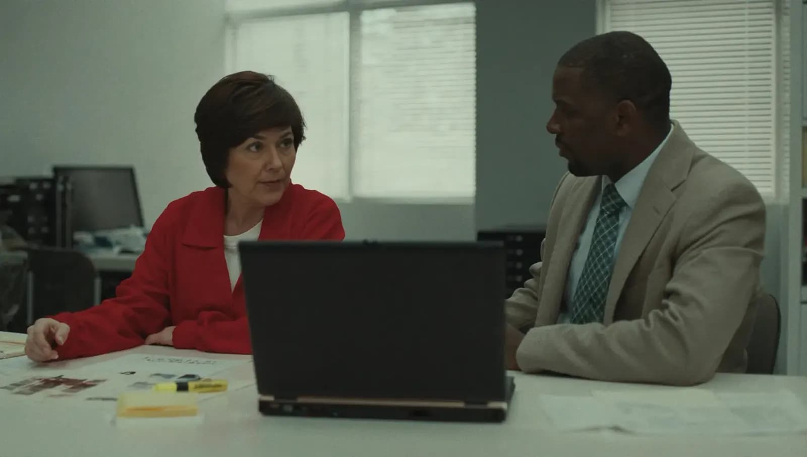 Two recruiters talking across a desk over a laptop and printed notes.